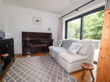 A living room with a sofa near a piano and large windows overlooking greenery at Ty Cerrig in Newport Pembrokeshire