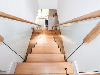 A staircase with wooden steps and glass side panels leading down to a room with a floor mat and cushions at Ty Cerrig in Newport Pembrokeshire
