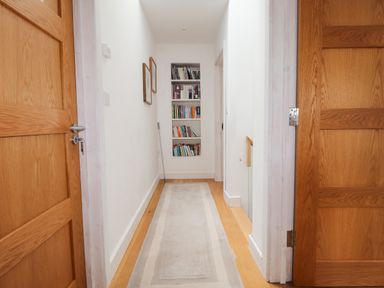 A hallway with wooden doors on either side a long rug on a wooden floor framed pictures on the wall and a built in bookshelf at Ty Cerrig in Newport Pembrokeshire