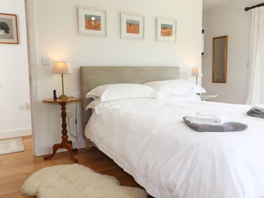 A bedroom with a double bed white bedding bedside tables with lamps and a sheepskin rug at Ty Cerrig in Newport Pembrokeshire