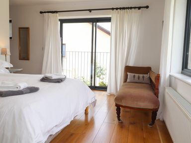 A bedroom with a bed with towels a chaise lounge a window with white curtains and wooden flooring at Ty Cerrig in Newport Pembrokeshire