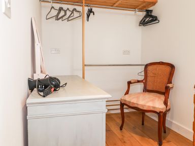 A dressing room with a white chest of drawers a mirror hairdryer coat hangers and a wooden chair with a cushioned seat at Ty Cerrig in Newport Pembrokeshire