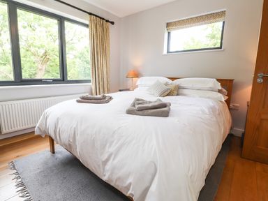 A bedroom with a double bed white bedding folded towels a lamp window with curtains and wooden floor at Ty Cerrig in Newport Pembrokeshire