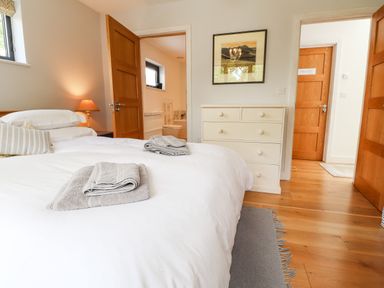 A bedroom with a white bedspread folded towels on the bed a dresser and an open door leading to a bathroom at Ty Cerrig in Newport Pembrokeshire