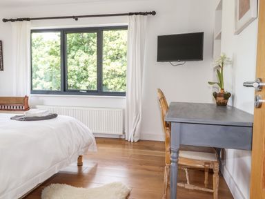 A bedroom with a bed folded towels on it a blue desk with a chair and a television mounted on the wall at Ty Cerrig in Newport Pembrokeshire