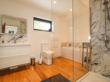 A bathroom with a sink and mirror a toilet a bathtub and a shower area with marble tiles and wooden floor at Ty Cerrig in Newport Pembrokeshire