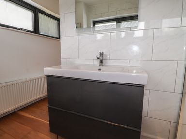 A bathroom sink with a cabinet below a mirror and a radiator near a window at Ty Cerrig in Newport Pembrokeshire