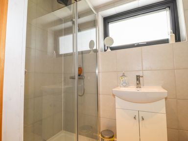 A bathroom with a glass shower enclosure, a white sink cabinet, and a window above the sink at Ty Cerrig in Newport Pembrokeshire