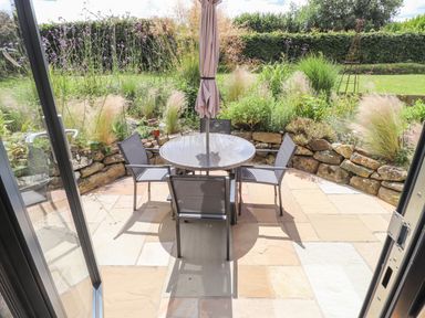 A patio with glass table and four chairs surrounded by plants and shrubs at Ty Cerrig in Newport Pembrokeshire