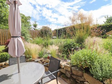 A garden patio with a round glass table umbrella and chairs surrounded by plants and stone wall at Ty Cerrig in Newport Pembrokeshire