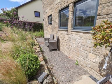 A gravel patio with two chairs next to a stone wall and a garden with plants and flowers at Ty Cerrig in Newport Pembrokeshire