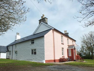 An exterior view of a large two-story house with white and pink walls a slate roof and outdoor seating on the front patio at Tremynydd Fawr in St Davids Pembrokeshire