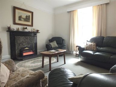 A living room with a fireplace a wooden coffee table leather couches and a cushioned armchair at Tremynydd Fawr in St Davids Pembrokeshire