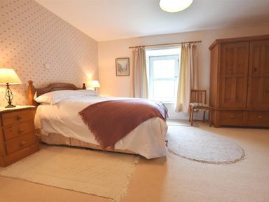 A bedroom with a double bed bedside tables lamps an armoire a chair a window and rugs at Tremynydd Fawr in St Davids Pembrokeshire