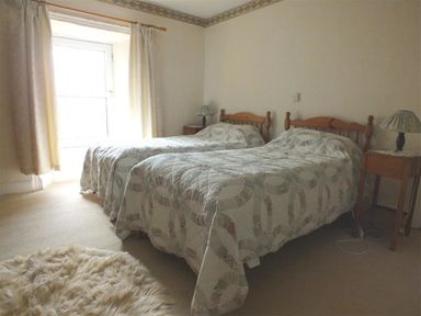 A bedroom with two single beds covered with patterned quilts two bedside tables with lamps and a window with curtains at Tremynydd Fawr in St Davids Pembrokeshire