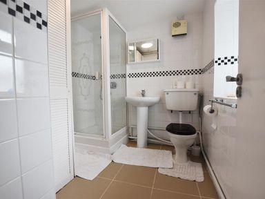 A bathroom with a shower, a pedestal sink, a toilet with a black seat, and white tiled walls with a black and white checkered border at Tremynydd Fawr in St Davids Pembrokeshire