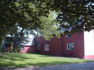 A red stone house with white framed windows surrounded by trees and grass at Tremynydd Fawr in St Davids Pembrokeshire