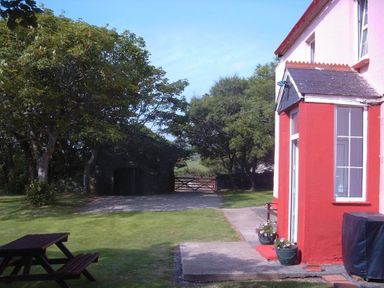 An outdoor area with a red and white building corner two flower pots a picnic table trees and a gate in the background at Tremynydd Fawr in St Davids Pembrokeshire