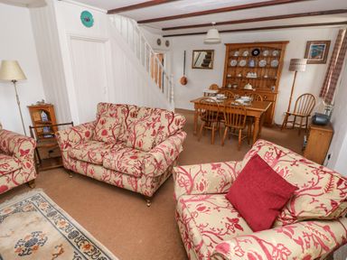 A living room with patterned sofas a dining table and chairs a wooden cabinet and staircase at Ty Canol in Mathry Pembrokeshire