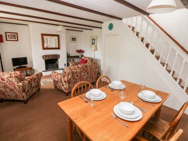 A dining table set for four and a sitting area with patterned sofas a fireplace and a television at Ty Canol in Mathry Pembrokeshire