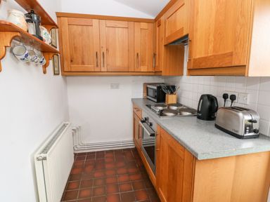 A kitchen with wooden cabinets a countertop with a toaster kettle microwave and stove and a shelf with cups and teapots at Ty Canol Mathry Pembrokeshire