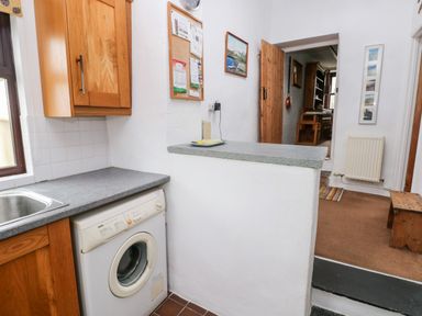 A kitchen area with a washing machine under a countertop and a wooden bench in an adjoining room at Ty Canol Mathry Pembrokeshire