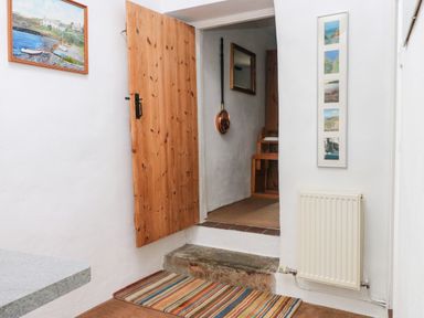 A wooden door open to a small step with a striped rug below a radiator on a white wall at Ty Canol Mathry Pembrokeshire