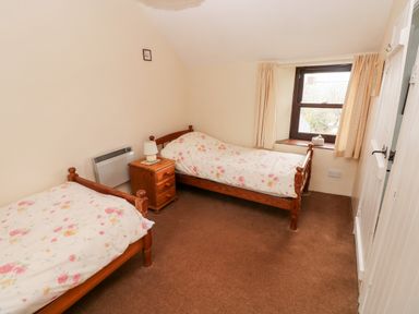 A bedroom with two single wooden beds a wooden nightstand with a lamp and a window with curtains at Ty Canol in Mathry Pembrokeshire