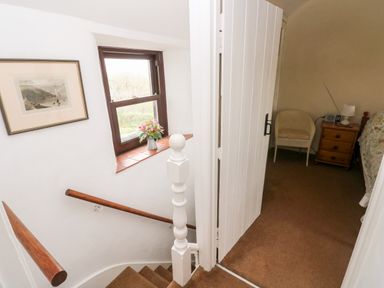 A staircase with wooden handrails and a window with flowers on the sill next to a bedroom with a chair bedside table and bed at Ty Canol in Mathry Pembrokeshire