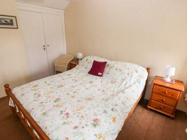 A bedroom with a double bed floral bedspread bedside tables with lamps a chair and a built in wardrobe at Ty Canol in Mathry Pembrokeshire