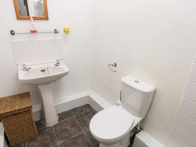 A bathroom with a toilet a pedestal sink a wicker laundry basket and a mirror at Ty Canol in Mathry Pembrokeshire