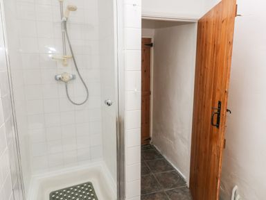 A shower area with white tiles and a wooden door opening to a hallway at Ty Canol in Mathry Pembrokeshire