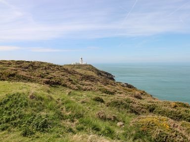 A coastal landscape with green hills and a white lighthouse on a cliff overlooking the ocean at Ty Canol in Mathry Pembrokeshire