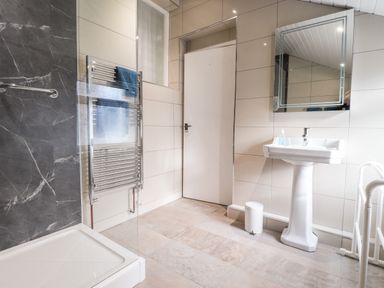 A bathroom with a shower area a heated towel rail with towels a pedestal sink a mirror and a waste bin at Meadowlands in Dinas Cross Pembrokeshire