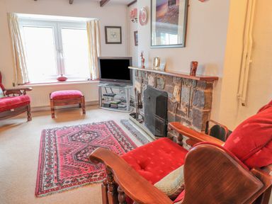 A sitting room with wooden armchairs with red cushions a stone fireplace a television and a window at Meadowlands in Dinas Cross Pembrokeshire