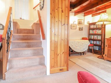A carpeted staircase next to a wooden bookcase and a table with a floral tablecloth at Meadowlands in Dinas Cross Pembrokeshire
