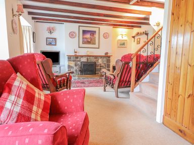 A living room with red armchairs a stone fireplace and a staircase at Meadowlands in Dinas Cross Pembrokeshire