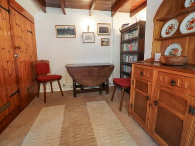 A room with a wooden folding table two red cushioned chairs a wooden cabinet with decorative plates and a bookshelf at Meadowlands in Dinas Cross Pembrokeshire