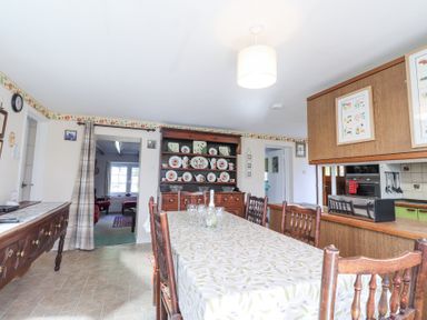 A dining room with a table set with glasses and a bottle wooden chairs and cabinets filled with plates at Meadowlands in Dinas Cross Pembrokeshire
