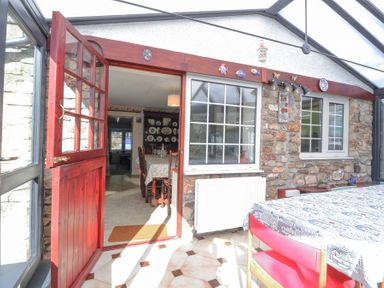A conservatory with a glass roof red door open to a dining room with a table and chairs at Meadowlands in Dinas Cross Pembrokeshire