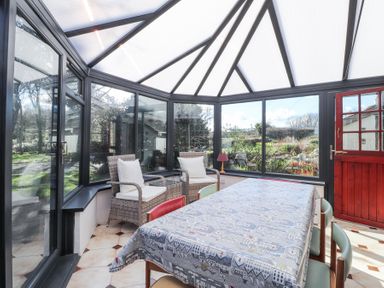A conservatory with a table covered with a cloth and chairs along with wicker armchairs and a side table at Meadowlands in Dinas Cross Pembrokeshire