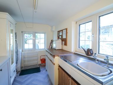 A utility room with a sink countertop wire shelf mop bucket and windows at Meadowlands in Dinas Cross Pembrokeshire