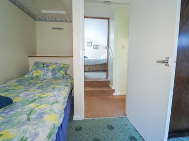 A small bedroom with a single bed and floral bedding next to a doorway leading to another room with a bed at Meadowlands in Dinas Cross Pembrokeshire