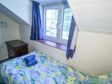 A small bedroom with a bed covered with floral bedding a folded towel on the bed a dark wooden nightstand and a window with blue curtains at Meadowlands in Dinas Cross Pembrokeshire