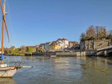 A riverside view with a docked sailboat and colorful buildings near a stone wall at Panteg Cardigan in Llangoedmor Cardigan