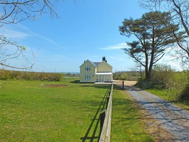 A yellow two-story house with a gravel driveway and fenced lawn under a blue sky at Sarnau in Efailwen Carmarthenshire