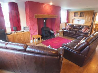 A living room with leather sofas a wood burner and wooden cabinets at Sarnau in Efailwen Carmarthenshire