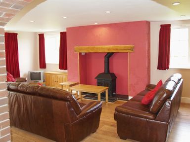 A living room with two brown leather sofas a wood burning stove and red curtains at Sarnau in Efailwen Carmarthenshire