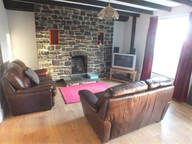 A living room with two brown leather sofas a stone fireplace a wooden floor and a television on a wooden stand at Sarnau in Efailwen Carmarthenshire