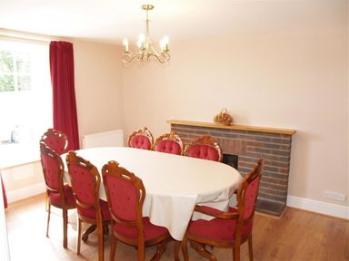 A dining room with an oval table covered with a white tablecloth and eight wooden chairs with red upholstery at Sarnau in Efailwen Carmarthenshire